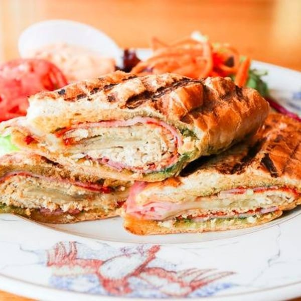Grilled panini sandwich with ham, cheese, and pesto, served with a side salad and dressing.