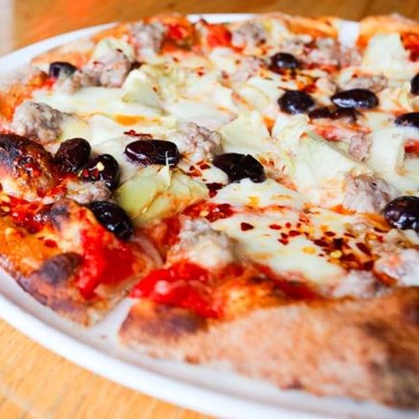 A Cleveland Park Bar & Grill pizza with sausage, olives, and artichoke hearts on a white plate.