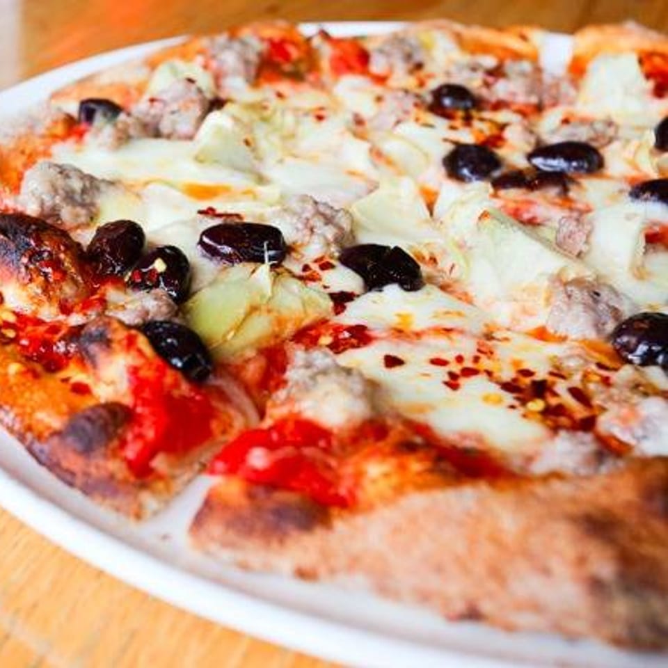 A Cleveland Park Bar & Grill pizza with sausage, olives, and artichoke hearts on a white plate.