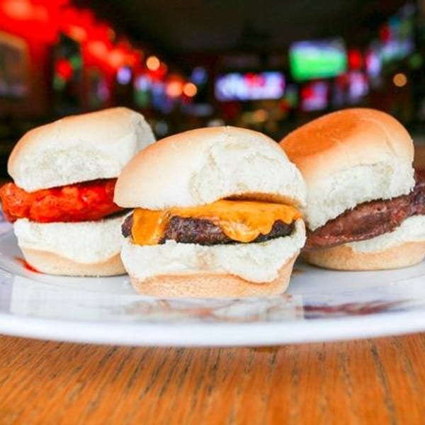 Three sliders on a white plate: one with red sauce, one with melted cheese, and one plain.