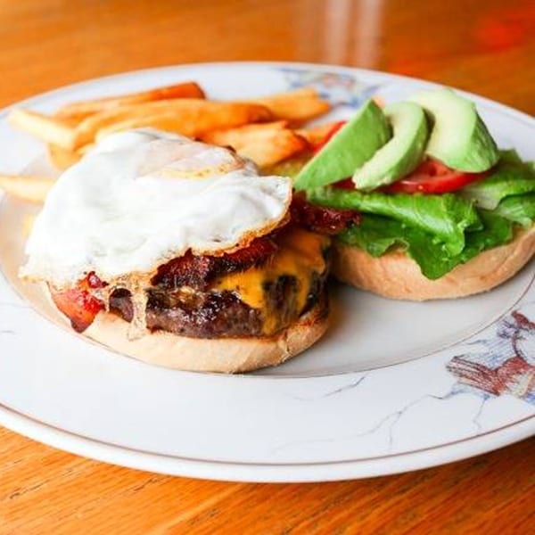 A burger with a fried egg, bacon, and cheese, with fries and an avocado burger.