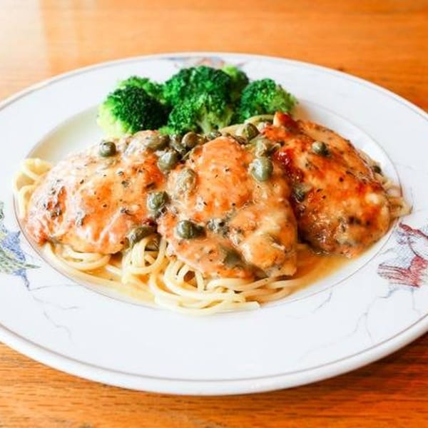 Chicken piccata with capers and sauce over spaghetti, served with a side of broccoli.